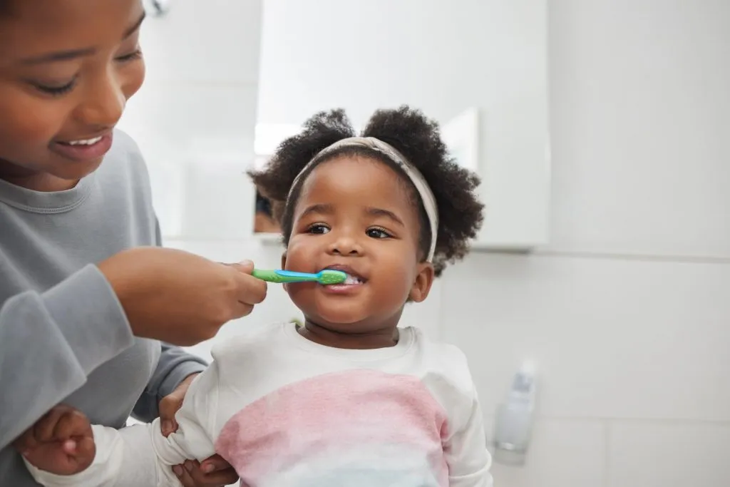Mom helping daughter brush teeth